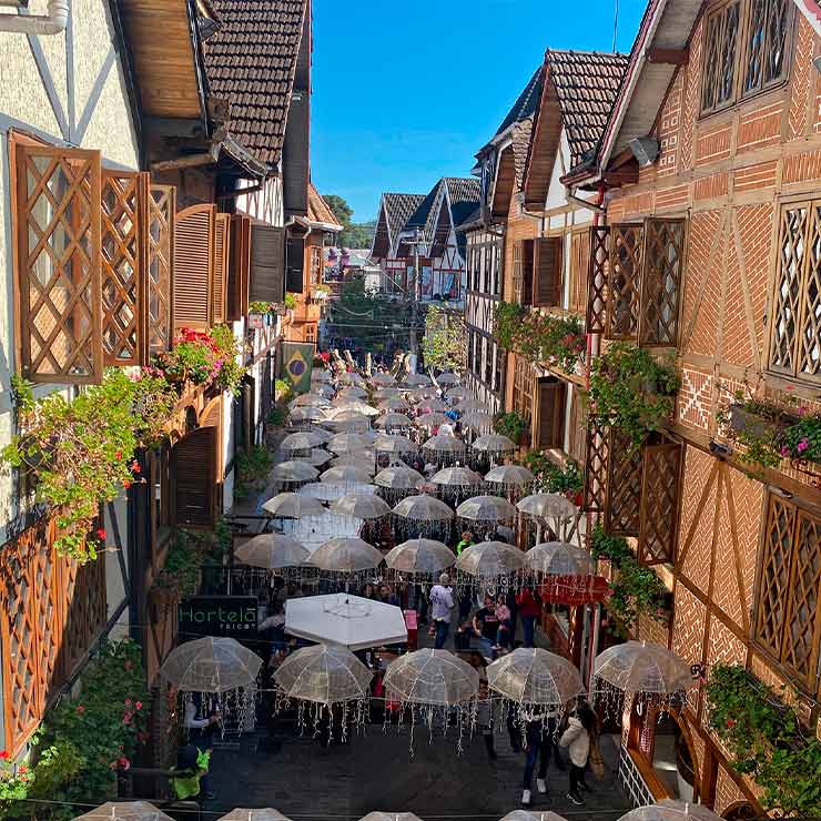 Vista encantadora de uma rua decorada com guarda-chuvas, rodeada por casas de estilo europeu e flores, ideal para visitas turísticas.